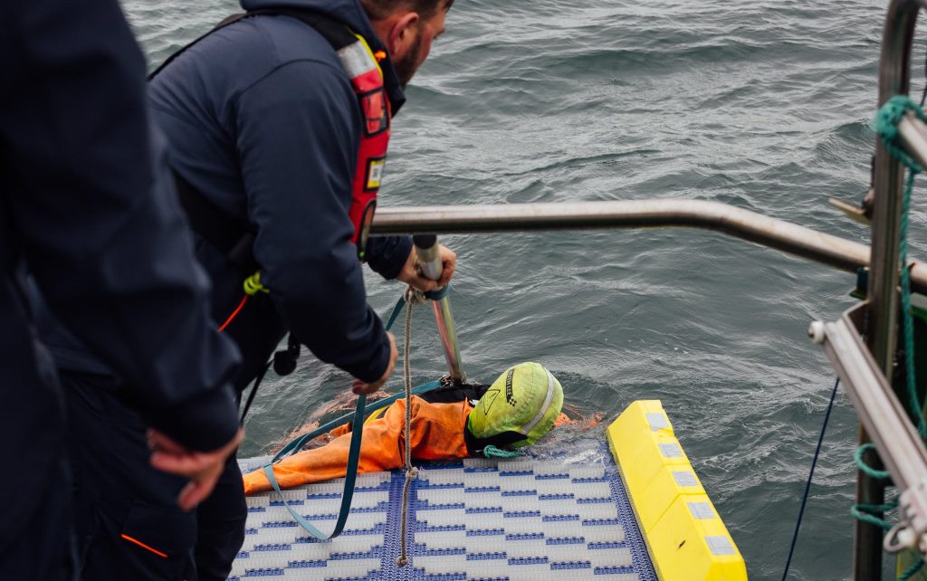 Crew on the SWIFT man-overboard recovery system pulling a training mannequin from the water during a recovery drill.