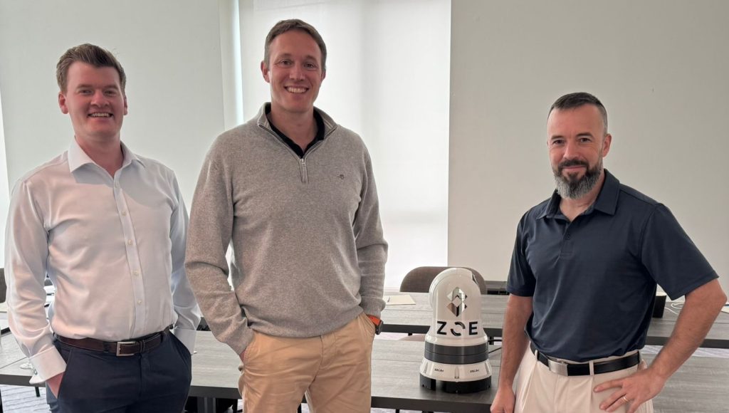 Zelim's Technical Lead Rory Hughes, CTO Doug Lothian, and Commander Matthew Mitchell standing together in a modern conference room with ZOE Intelligent Detection system visible on the table.